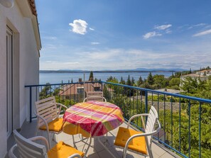 Un balcone con tavolo e sedie, vista su un corpo d'acqua e colline lontane.