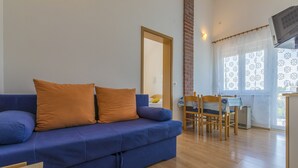 Un soggiorno con un divano blu, due cuscini arancioni, un tavolo da pranzo in legno con sedie e una zona cucina con un fornello.