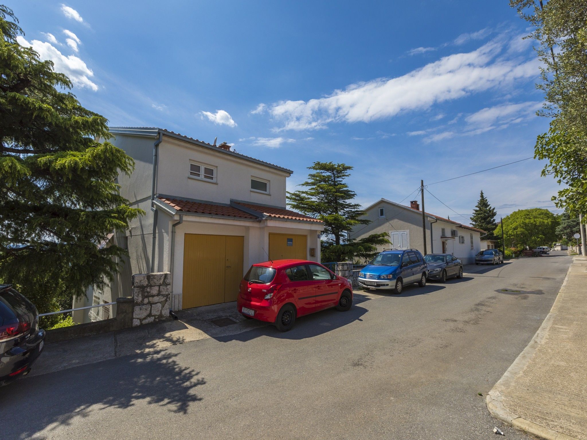Une rue résidentielle bordée de maisons, de voitures garées et d’arbres.