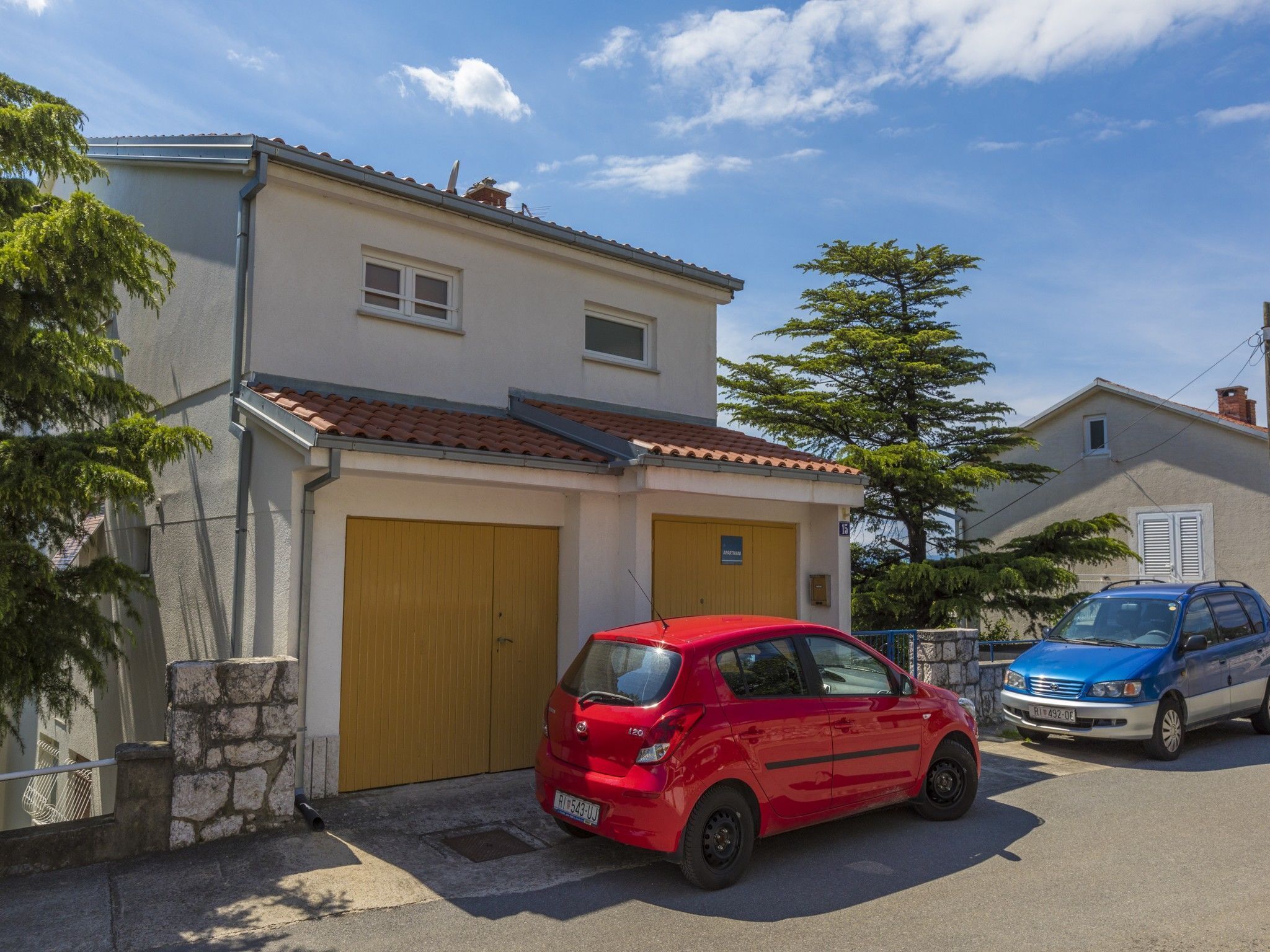 A two-story house with a garage, a red car parked in front, and a blue car parked in the driveway.
