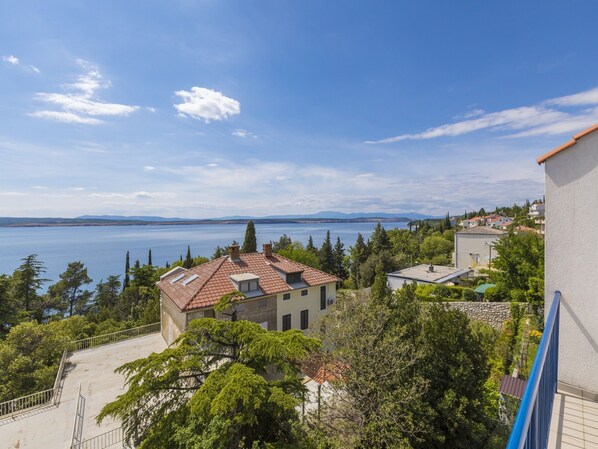 A coastal residential area with houses, a clear sky, and a large body of water in the background.