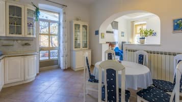 A dining area with a round table and chairs, a kitchen with cabinets, and a view through a window.