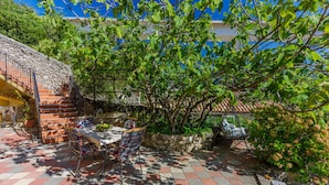 A patio with a table and chairs, surrounded by stone walls and greenery. - Apartment Piano (Crikvenica)