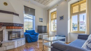 A living room with a fireplace, a blue armchair, a grey sofa, and a television. - Apartment Piano (Crikvenica)