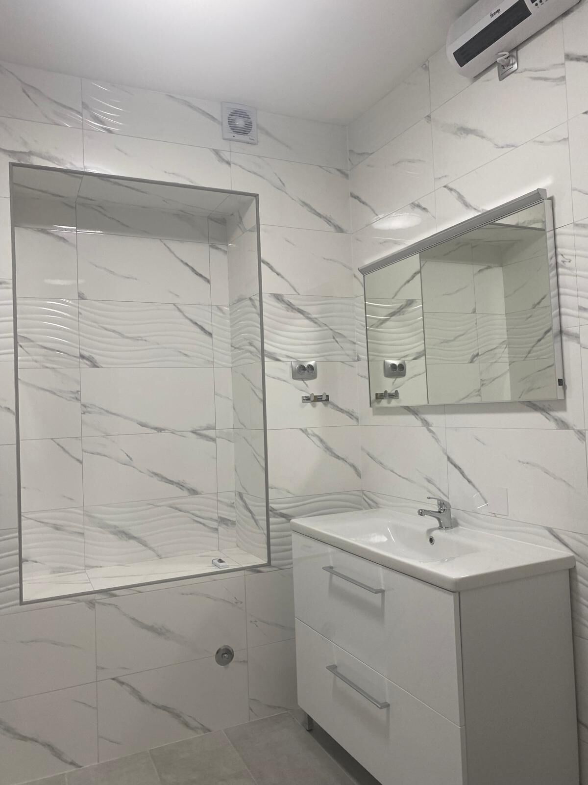 A bathroom with a shower, a sink, a mirror, and a wall-mounted air conditioner.