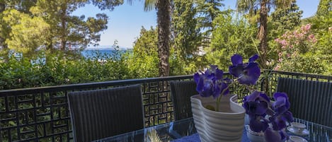 A balcony with a glass table, a white vase with purple flowers, and a clear glass bowl.