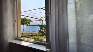 Une fenêtre donnant sur un jardin et un bâtiment situé de l’autre côté d’une étendue d’eau.