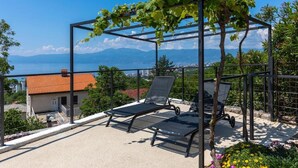 Une terrasse avec deux chaises longues, une pergola couverte de vignes et une vue sur la ville et les montagnes.