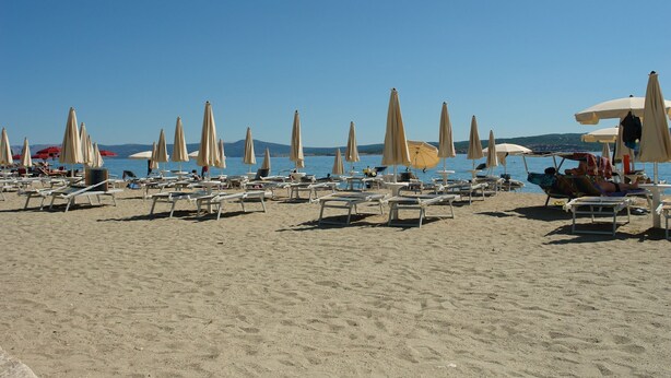 Una spiaggia con file di lettini e ombrelloni, un cielo sereno e un mare calmo sullo sfondo.