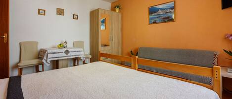 Une chambre avec un grand lit, une armoire en bois, un bureau avec une chaise et une petite table avec une plante.