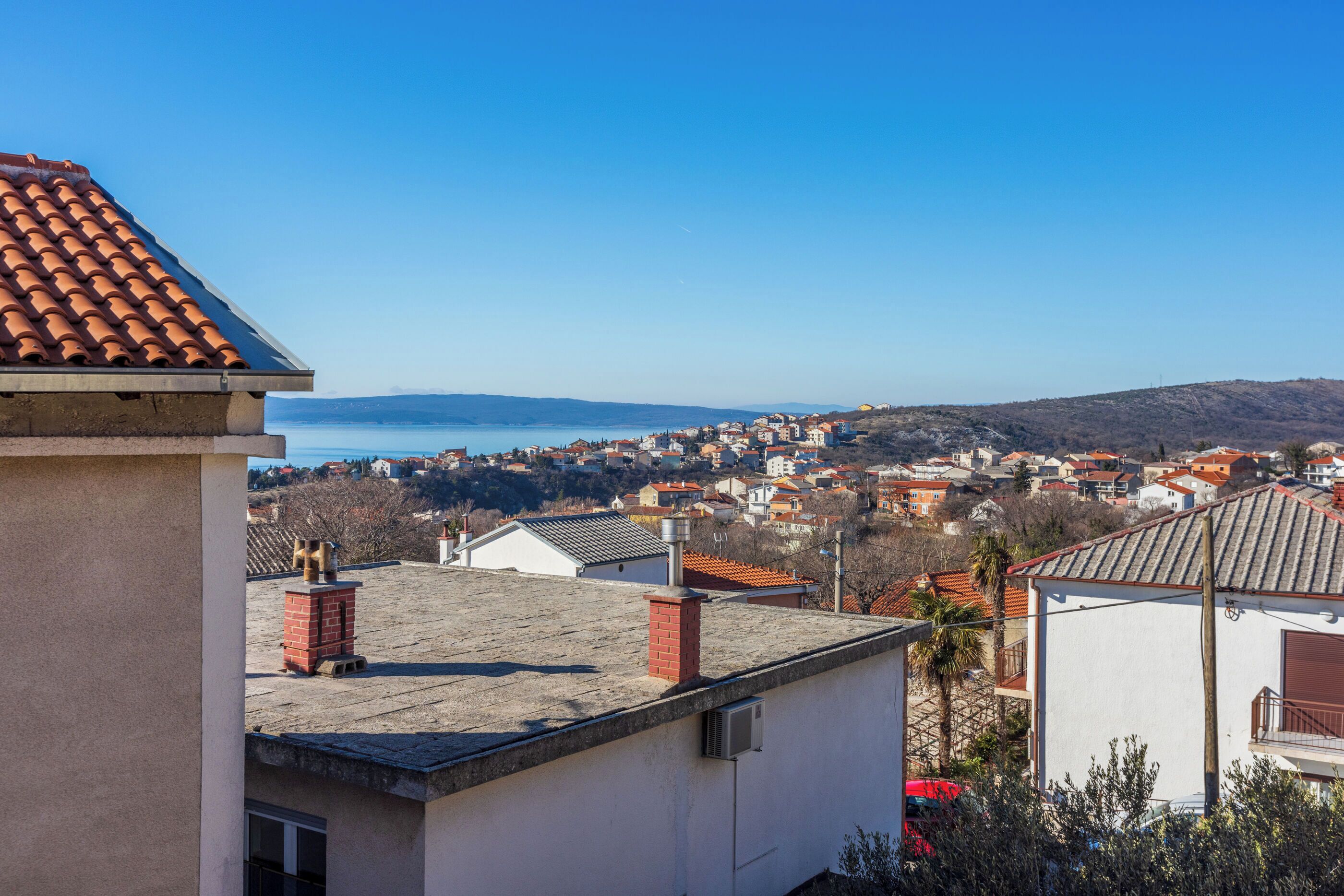 Une ville côtière aux bâtiments aux toits de tuiles rouges, sous un ciel bleu azur, offrant une vue sur la mer.