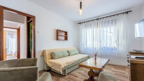 Una sala de estar acogedora con un sofá, dos sillones, una mesa de centro de madera y un televisor sobre un mueble de madera.
