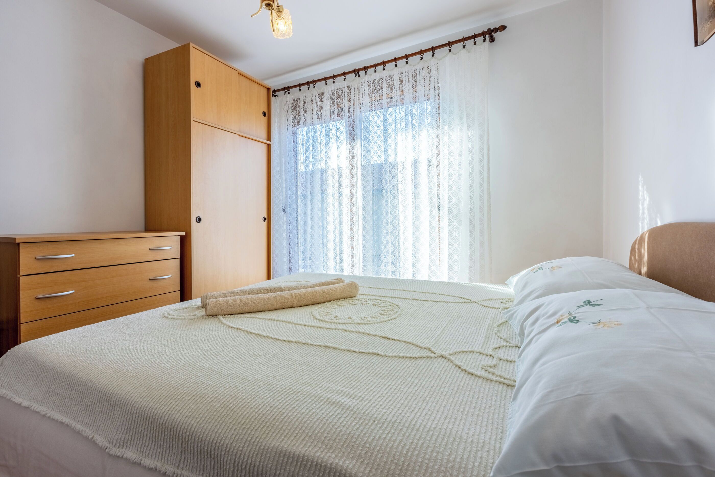 Un dormitorio con cama, armario de madera y ventana con cortinas estampadas.