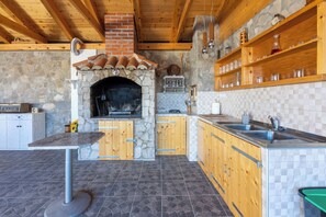 A rustic kitchen with a stone fireplace, wooden cabinets, and a tiled backsplash. - Apartments Josip (Novi Vinodolski)