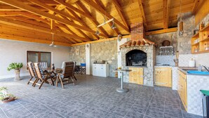Un área de cocina al aire libre con chimenea de piedra, vigas de madera en el techo y una mesa de comedor con sillas.