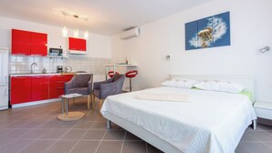 Una habitación de hotel moderna con una cama grande, una zona de comedor con armarios rojos y una cocina.