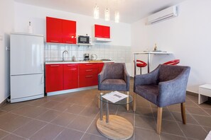 Eine moderne Küche mit roten Schränken, einem weißen Kühlschrank und einer Essecke mit zwei grauen Stühlen und einem kleinen Tisch.
