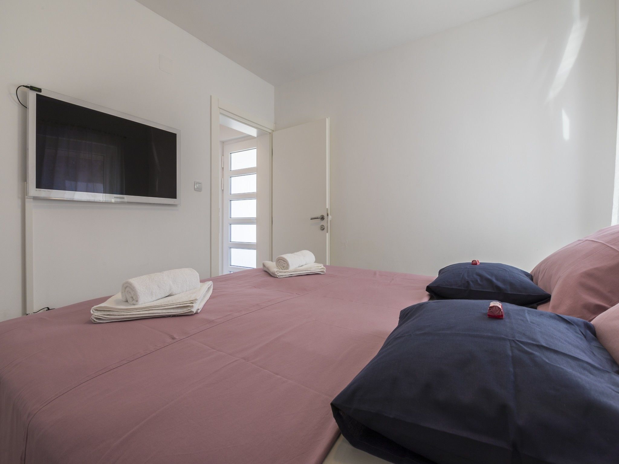 A bedroom with a bed, pillows, and a TV on the wall.