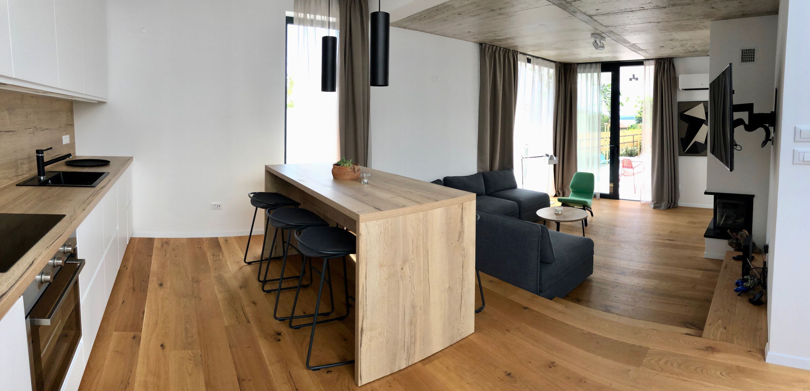 Una cocina moderna con una isla de madera, taburetes de bar y un comedor con sofá y una pequeña mesa.