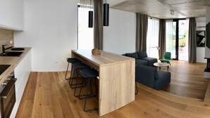 Une cuisine moderne avec un îlot central en bois, des tabourets de bar et un coin repas comprenant un canapé et une petite table.