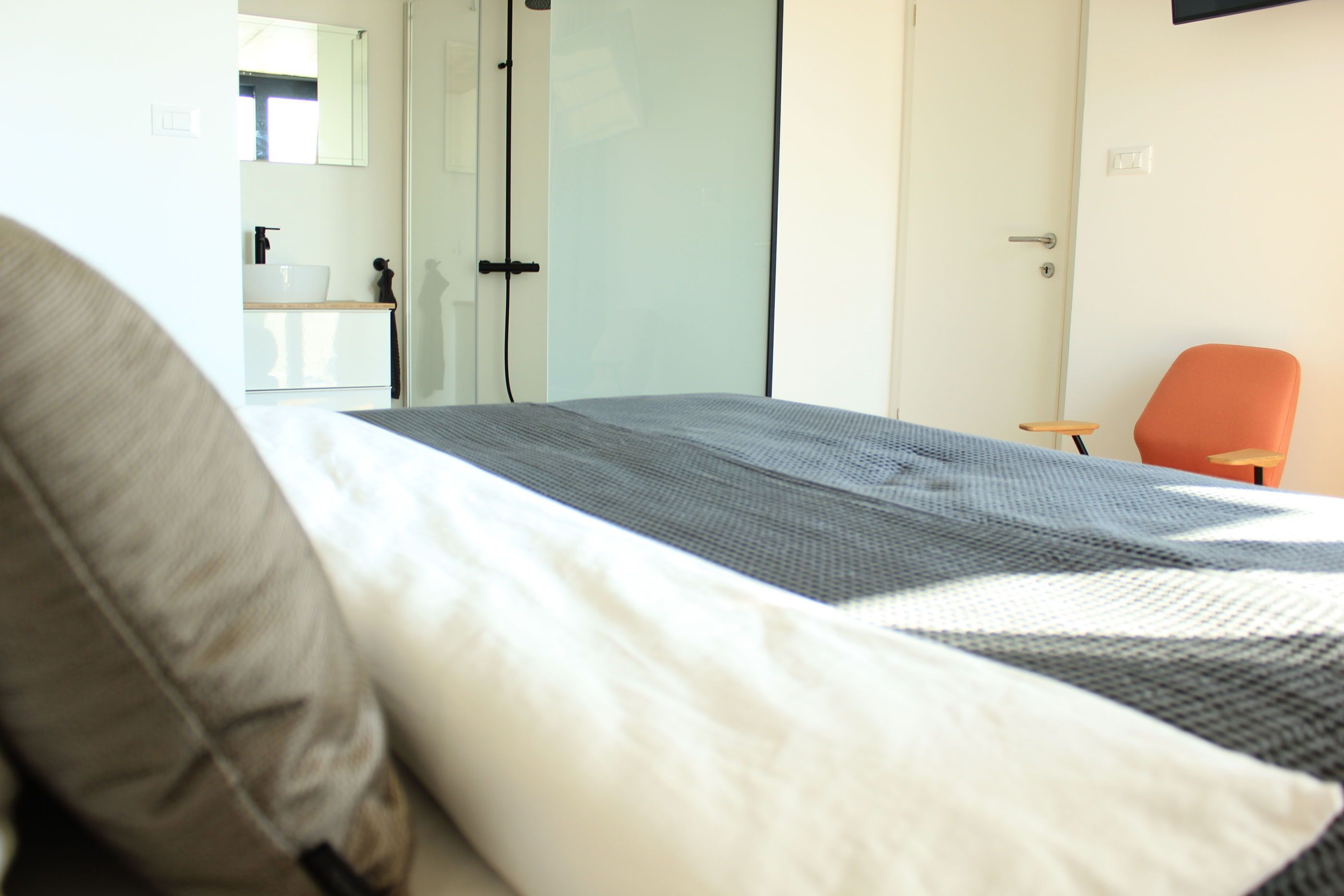 Un dormitorio con cama, una silla, un baño con lavamanos y una puerta.