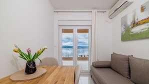 Ein modernes Wohnzimmer mit Holztisch, einer Couch und Blick durch eine Glastür auf einen Balkon.