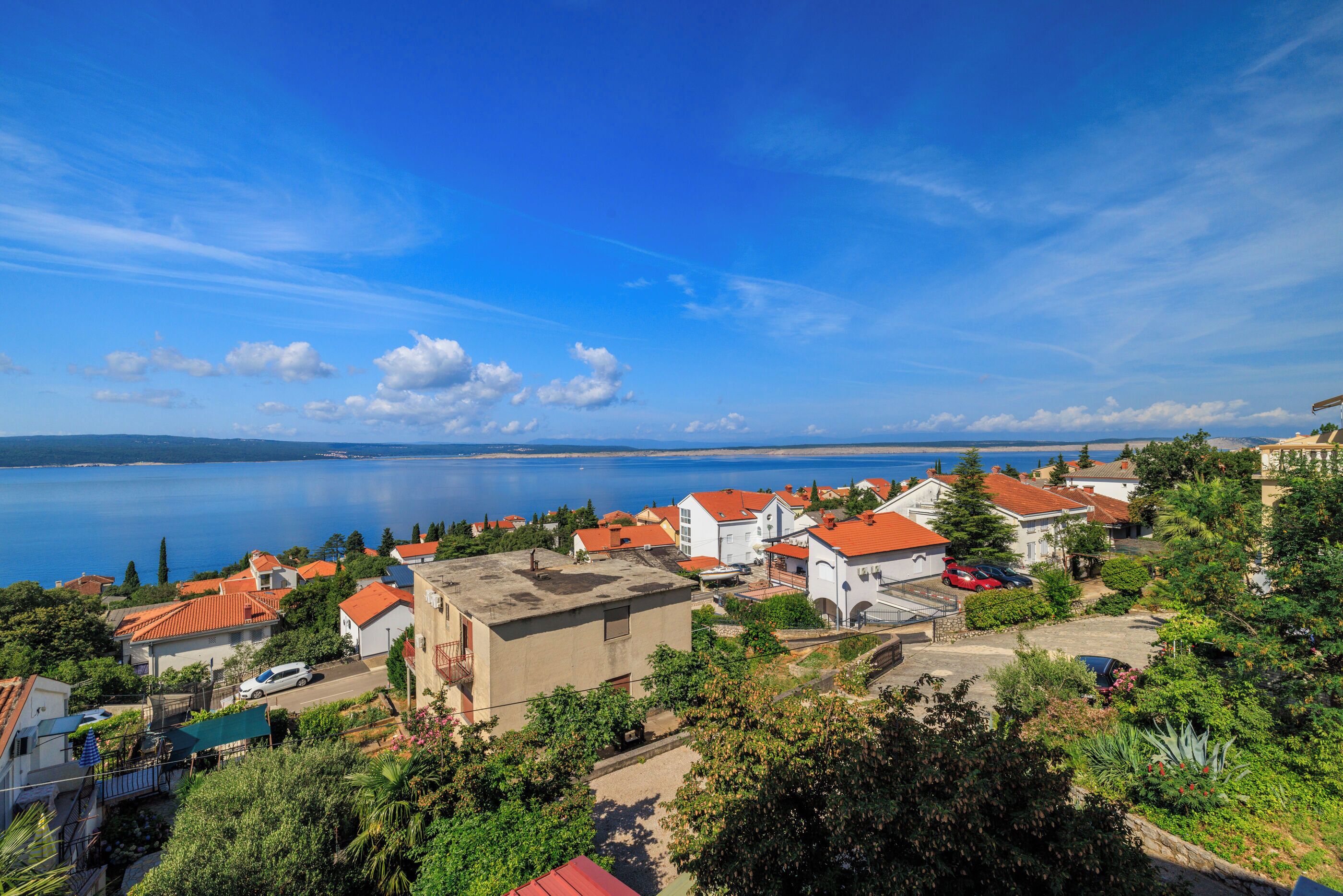 Un pueblo costero con casas de techo rojo, un cielo azul despejado y vistas al mar.