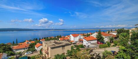 Un pueblo costero con casas de techo rojo, un cielo azul despejado y vistas al mar.