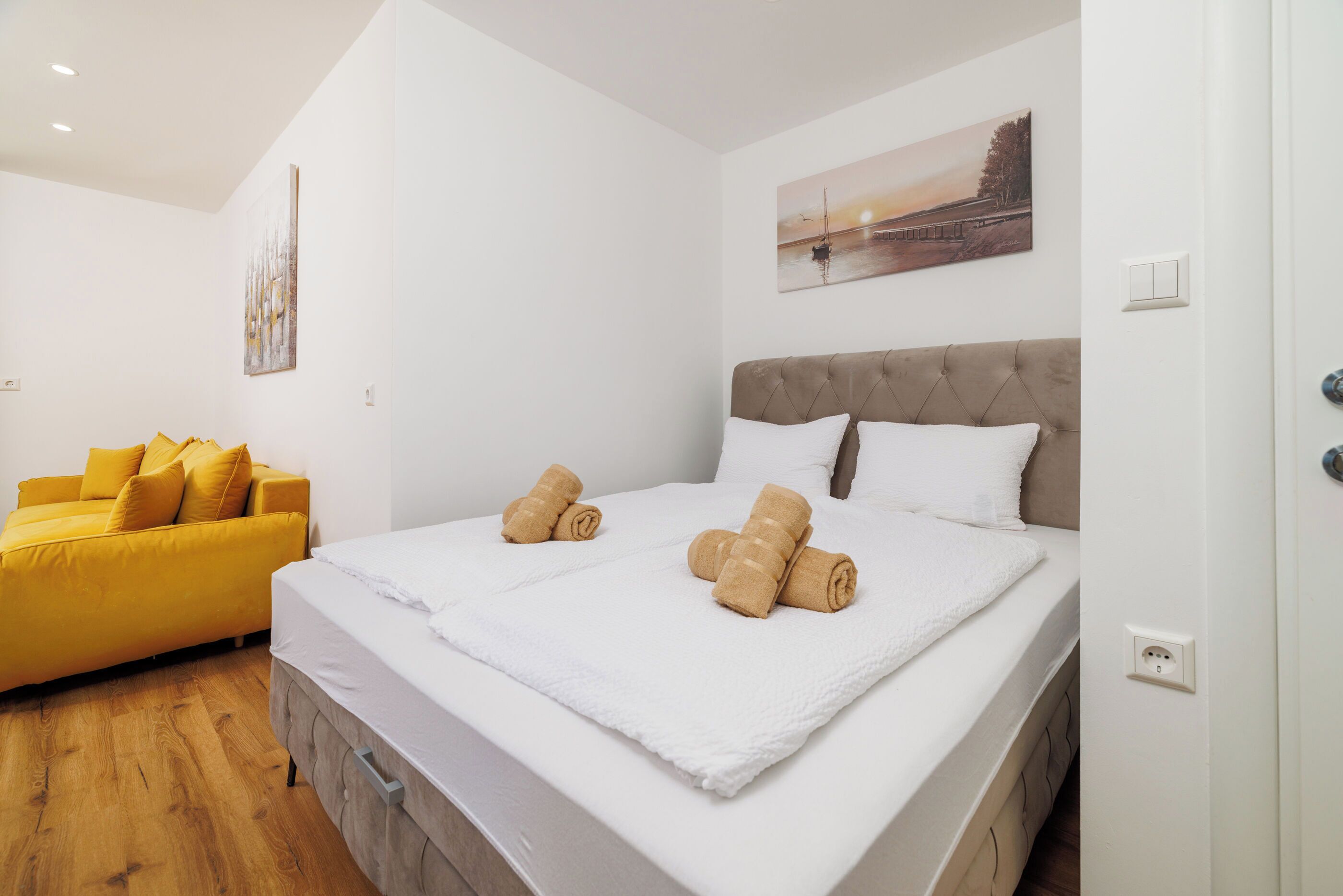A bedroom with a bed, a yellow sofa, and a painting on the wall.