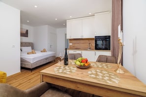 A compact room with a bed, a dining table with a fruit bowl, a bottle, and a candle.