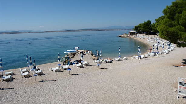 Ein Strand mit Liegen und Sonnenschirmen, ein klarer Himmel und ruhiges Meer.