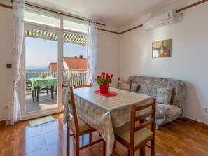 Quarto com uma mesa de jantar, cadeiras, um sofá e vista para o mar através de uma porta deslizante.