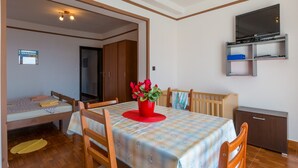 Una habitación compacta con una mesa de comedor, sillas, un televisor montado en la pared y una cama en una esquina.