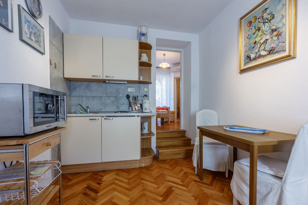 Une cuisine compacte équipée d’un four à micro-ondes, d’un évier et de placards, un coin repas avec une table et des chaises, et un escalier menant à une autre pièce.