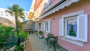 A pink building with white shutters, a stone wall, and a tiled patio with a bench and chairs. - Apartments Villa 7 (Crikvenica)