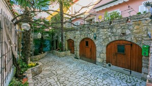 A courtyard with stone flooring, wooden doors, and a stone wall. - Apartments Villa 7 (Crikvenica)