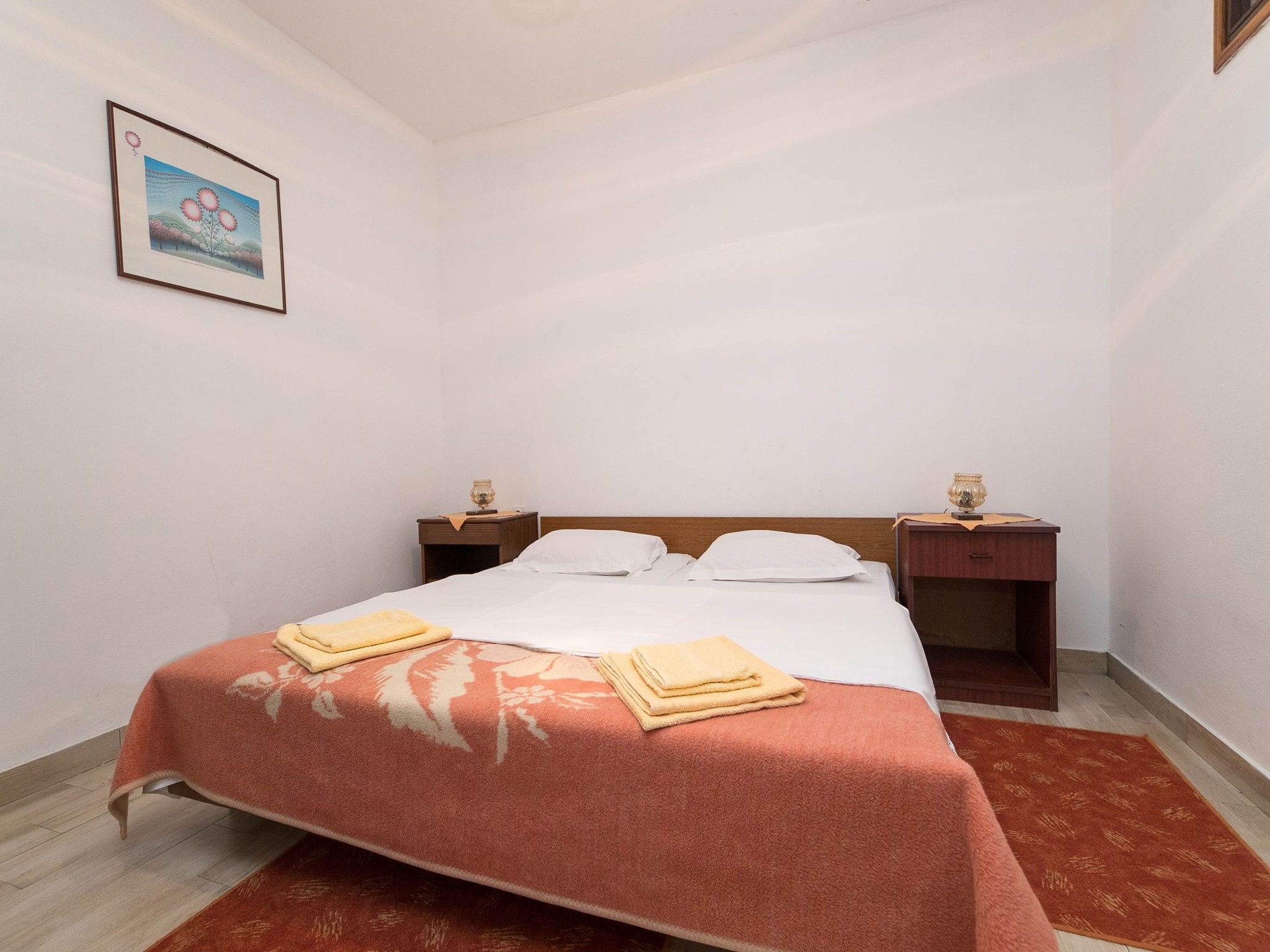 Une chambre d’hôtel avec un lit, deux tables de chevet, un tableau encadré au mur et un tapis rouge à motifs.