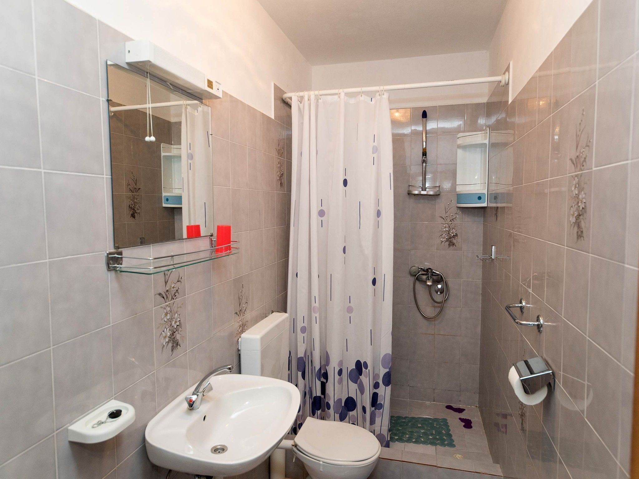A bathroom with a sink, toilet, shower, and a mirror.
