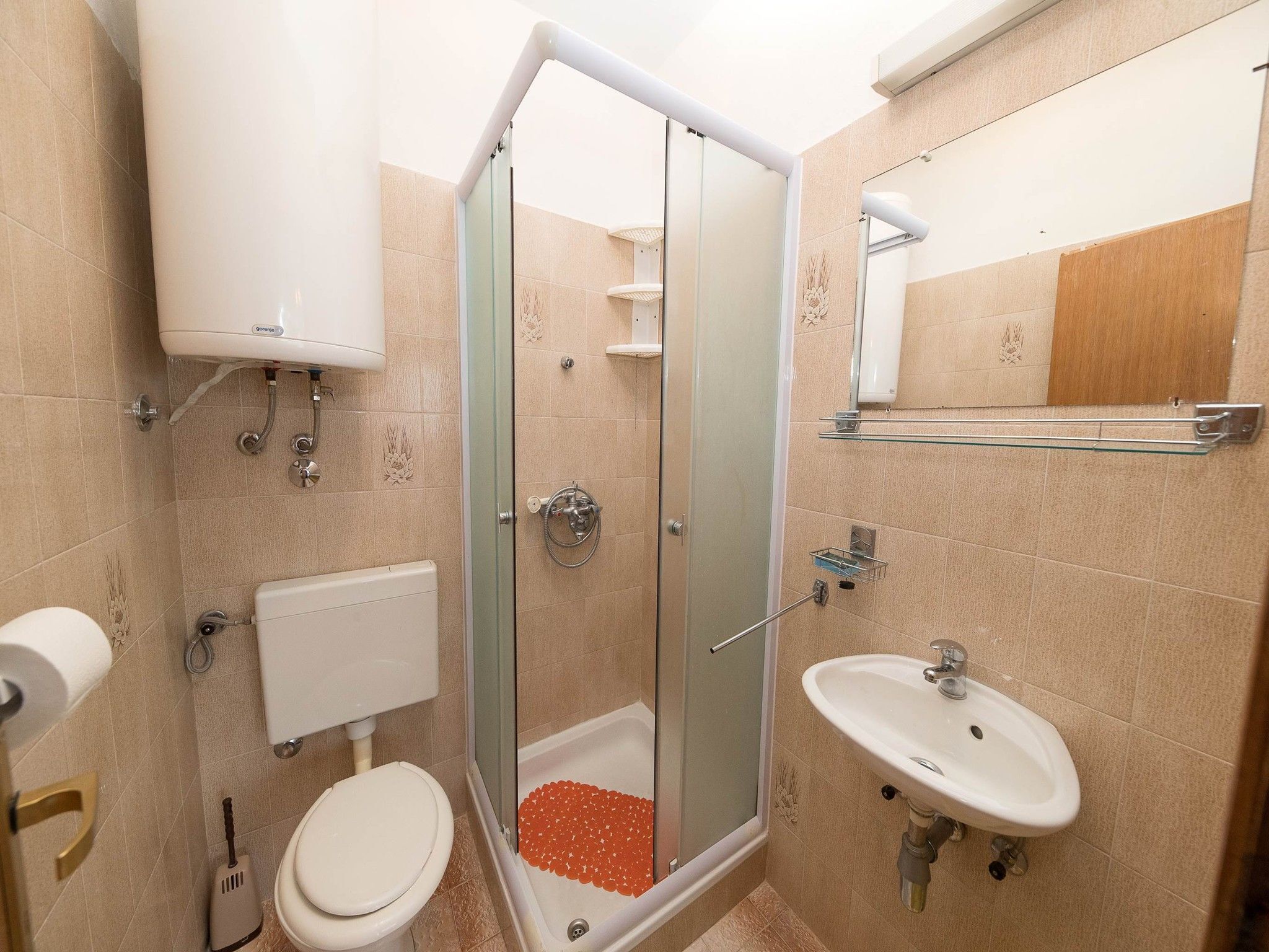 Egy fürdőszoba, amelyben üvegfalas zuhanyzó, WC, mosdókagyló és törölközőtartó található.