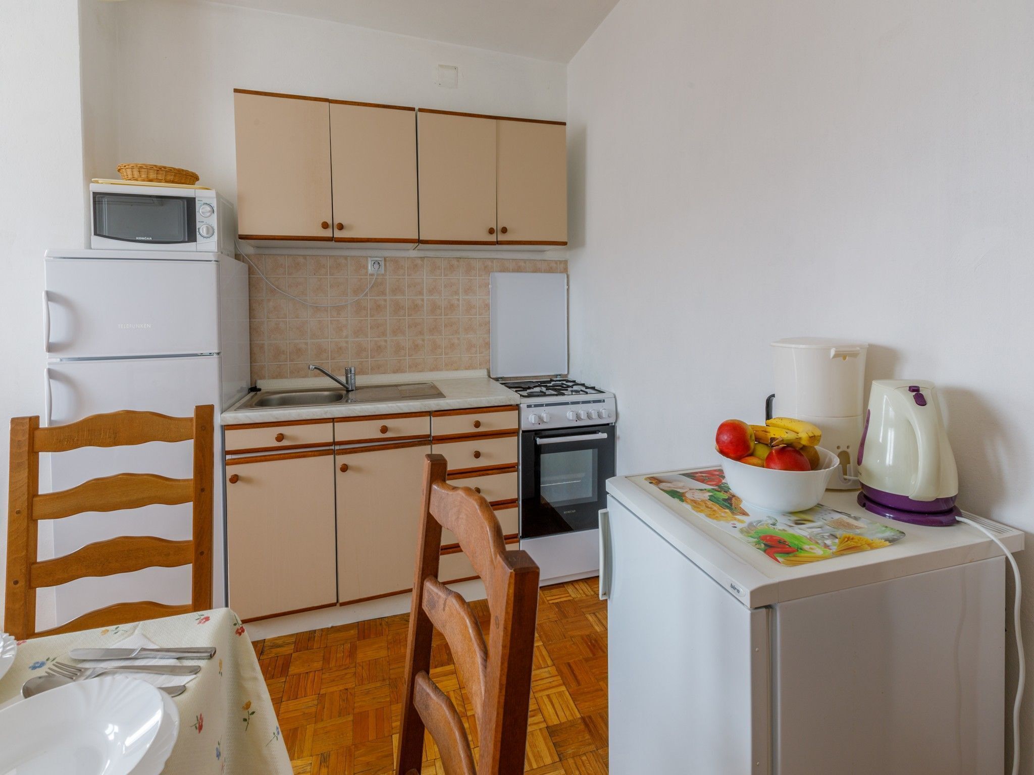 A compact kitchen with basic appliances, a dining area with a wooden chair, and a small table.