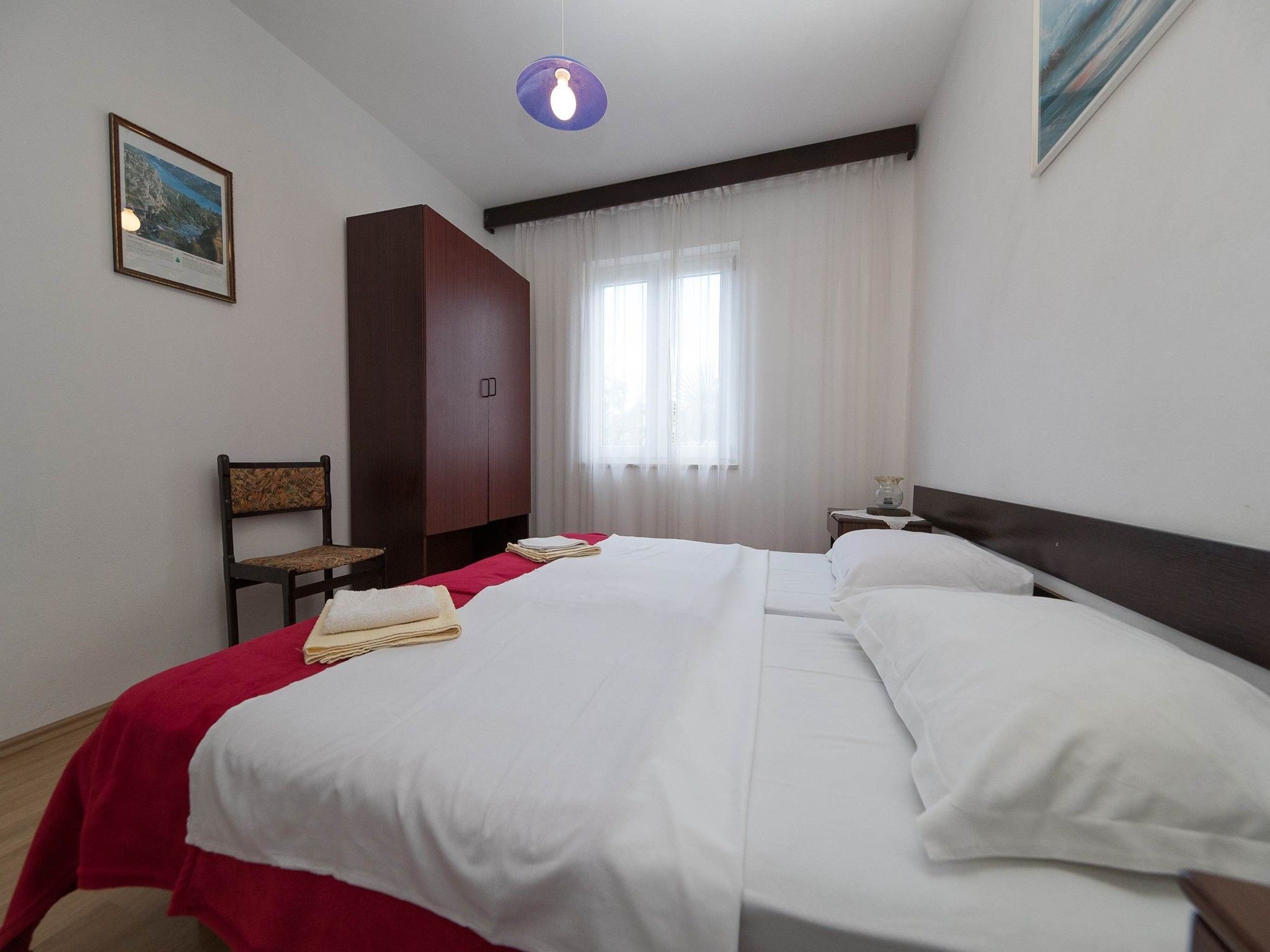 Habitación de hotel con una cama grande, un armario de madera, una silla, un escritorio con lámpara y un cuadro en la pared.
