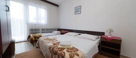 A hotel room with a large bed, two bedside tables, a nightstand, a window with sheer curtains, and a ceiling light fixture.