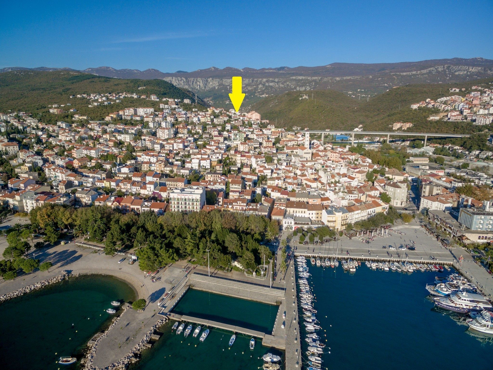 An aerial view of a coastal town with a marina, dense residential area, and a prominent yellow arrow pointing to a specific location.