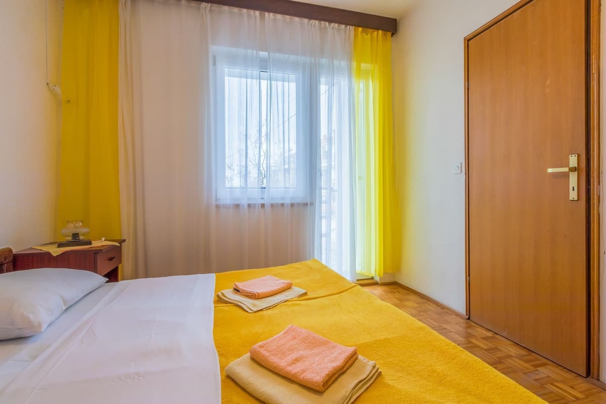 A hotel room with a bed, a nightstand, a wooden wardrobe, and a window with sheer curtains.