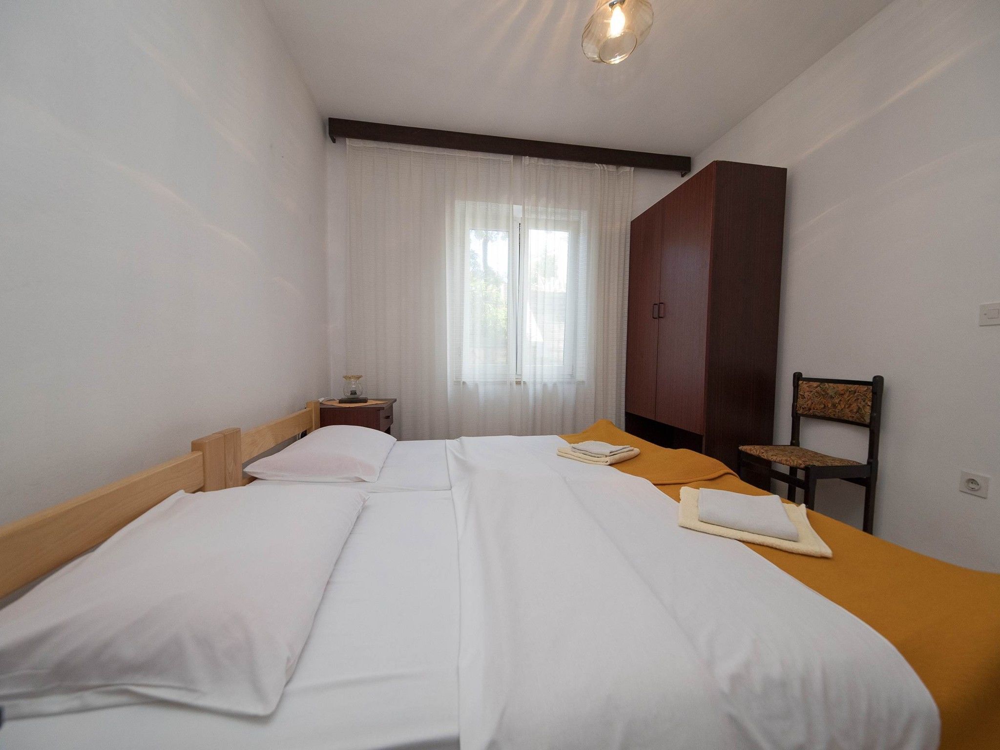 A hotel room with two beds, a wooden headboard, a nightstand, a chair, and a wardrobe.