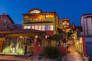 A multi-story hotel with a balcony, a gated entrance, and a well-lit facade.
