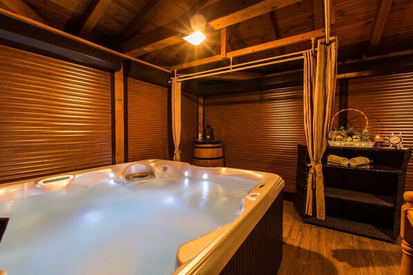 A hot tub in a wooden cabin with a rustic interior, a shelf with towels, and a lantern. - Apartments Ana Lorena (Crikvenica)