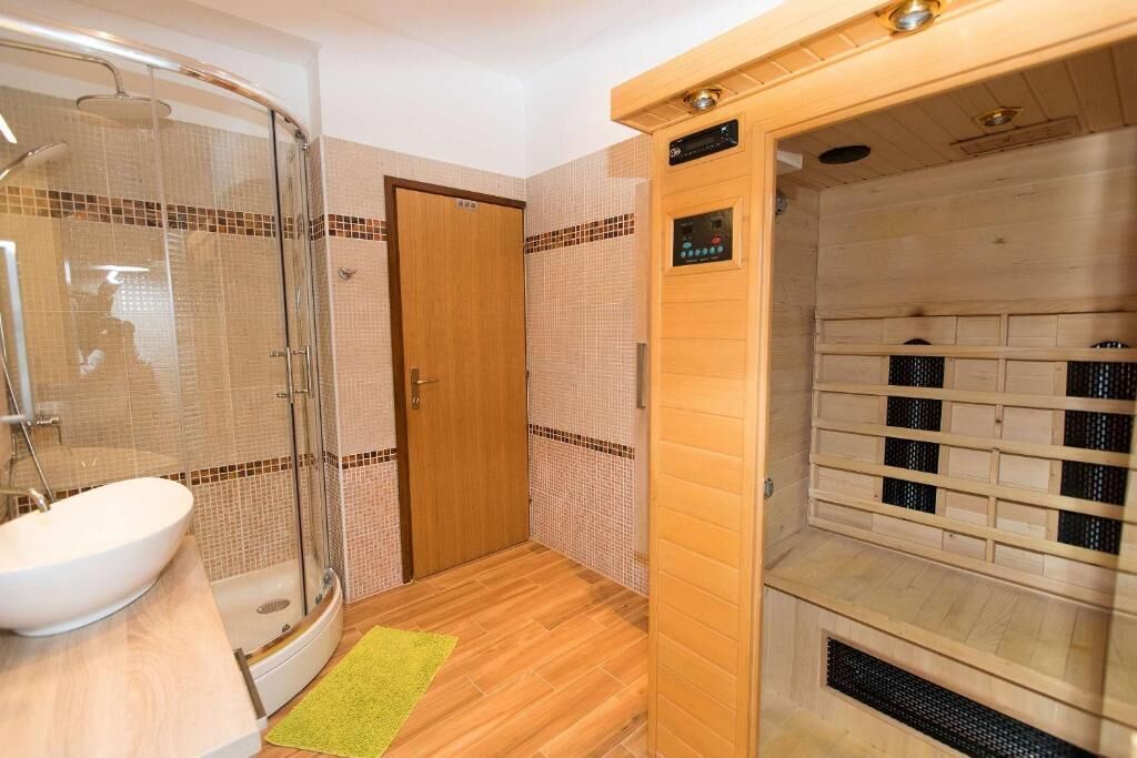 Un baño con cabina de ducha de vidrio, tocador de madera con lavabo y zona de sauna con panel de control.
