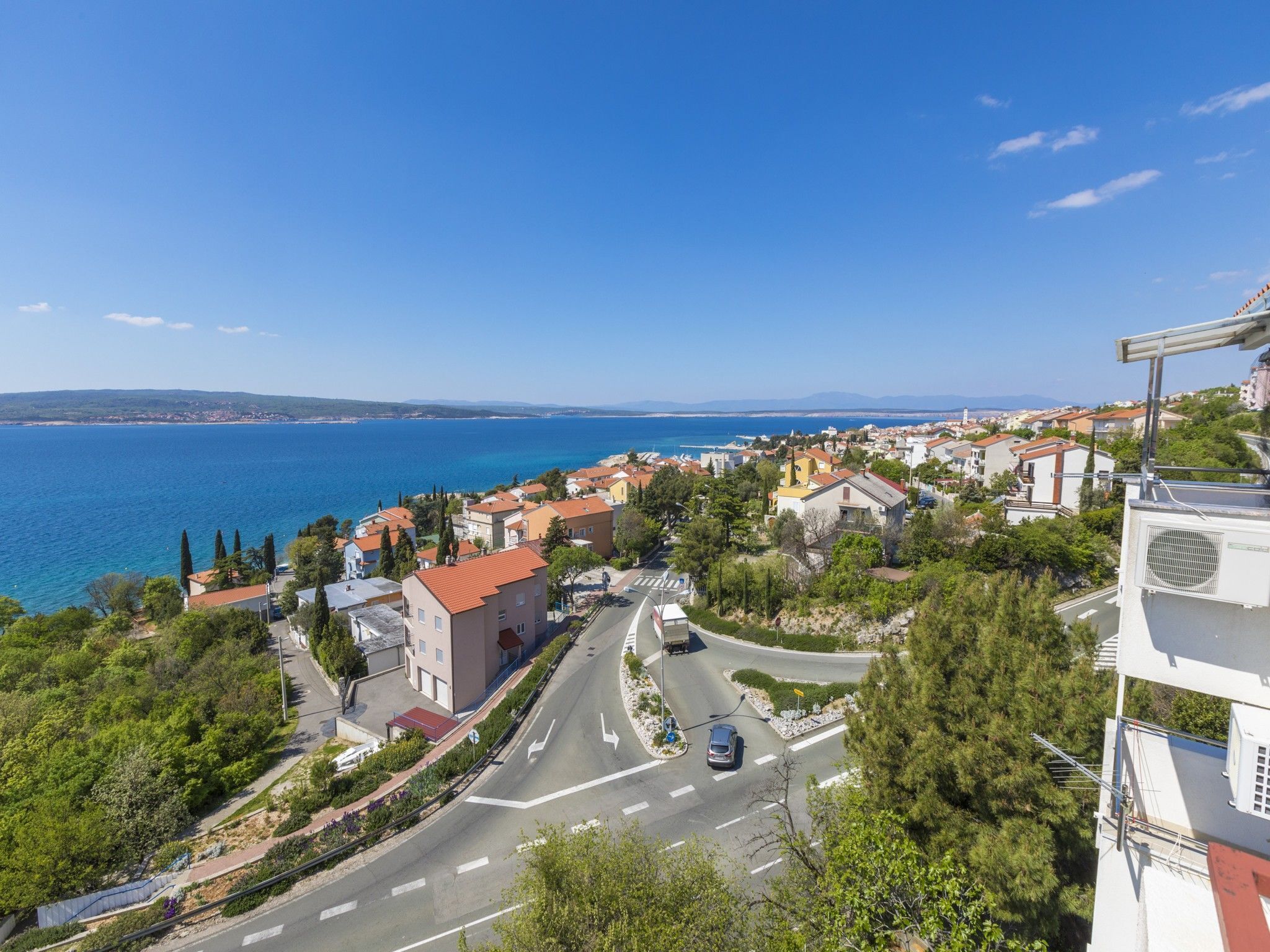 A coastal town with a road curving through it, buildings with red roofs, and a clear view of the sea.