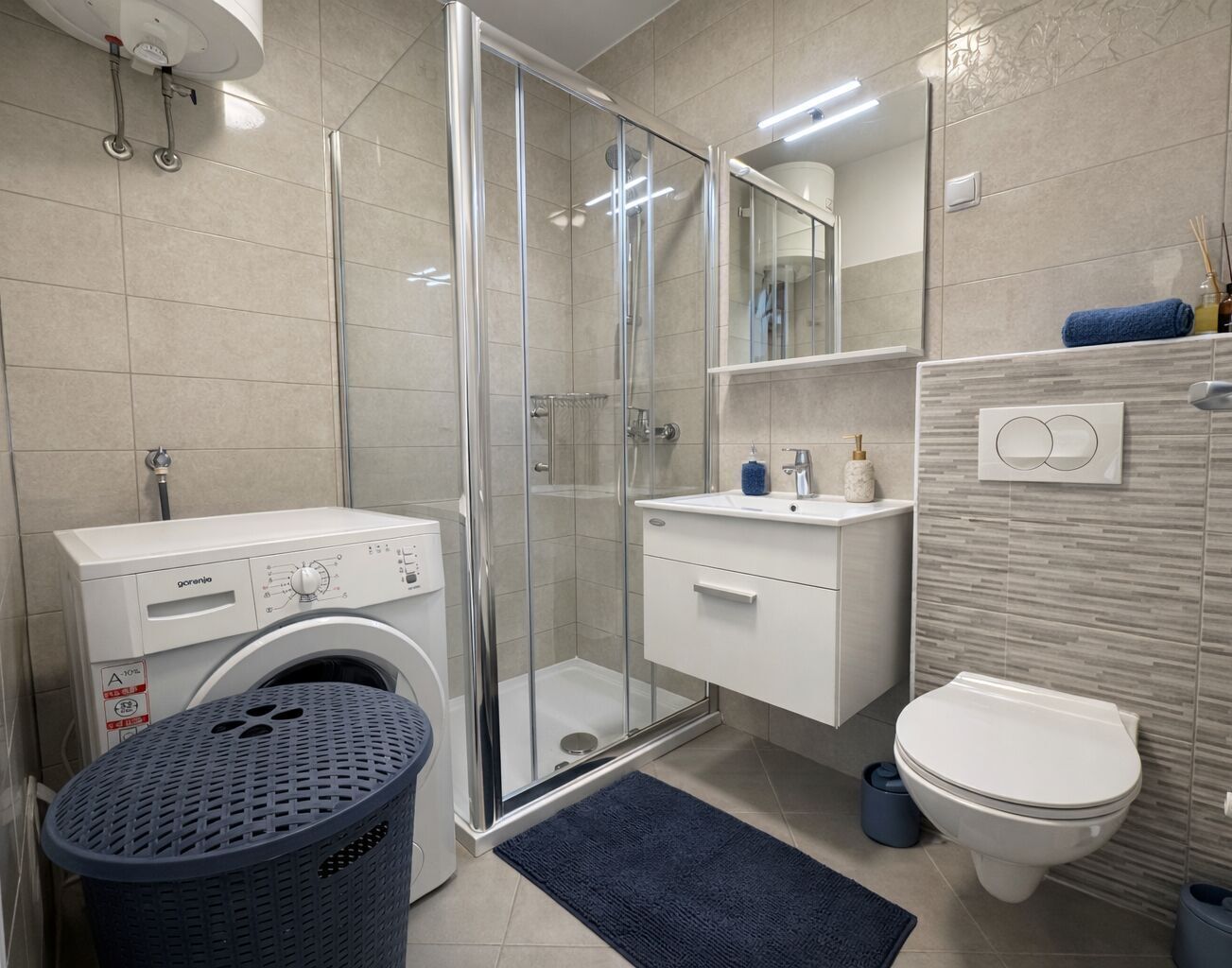 A modern bathroom with a glass-enclosed shower, a washing machine, a toilet, and a sink with a mirror above it.